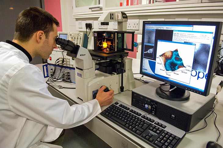 Scientist looking through a microscope with VDU display